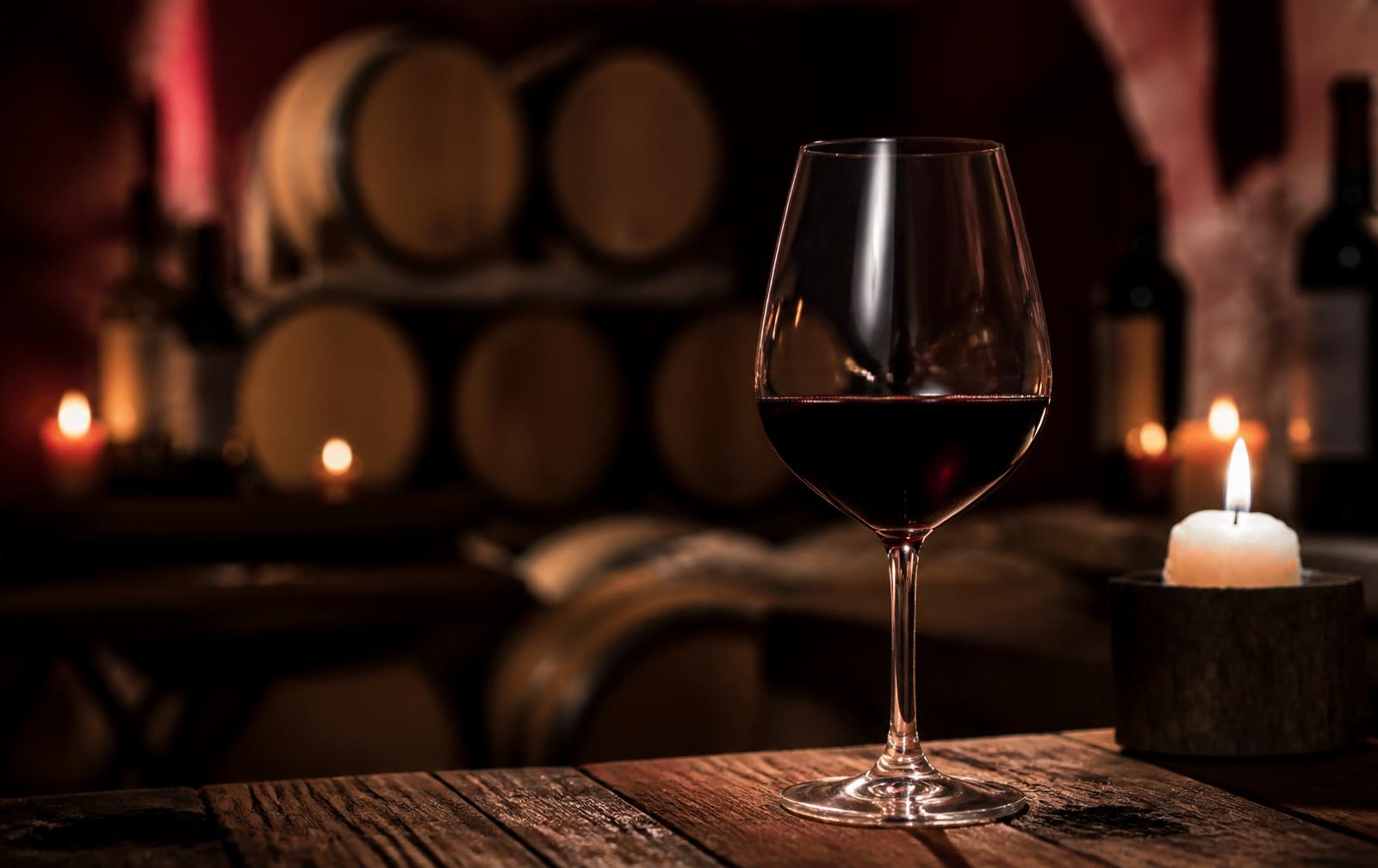 A glass of red wine on an oak table in a candlelit cellar
